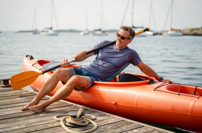 Homme glissant depuis un ponton dans un kayak gonflable orange, méthode d'embarquement latéral en marina